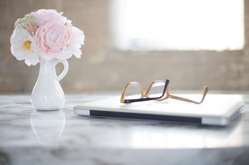 Free Image of Elegant eyeglasses resting on a closed laptop, with flowers nearby. 