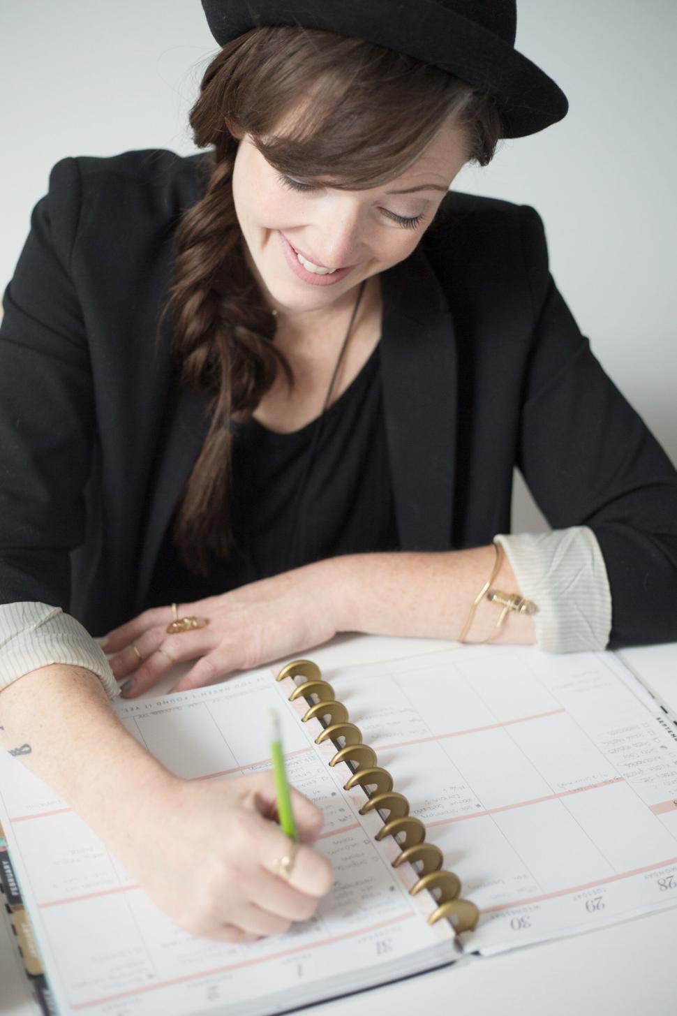 Free Image of Person writing in planner with green pencil, wearing black hat. 