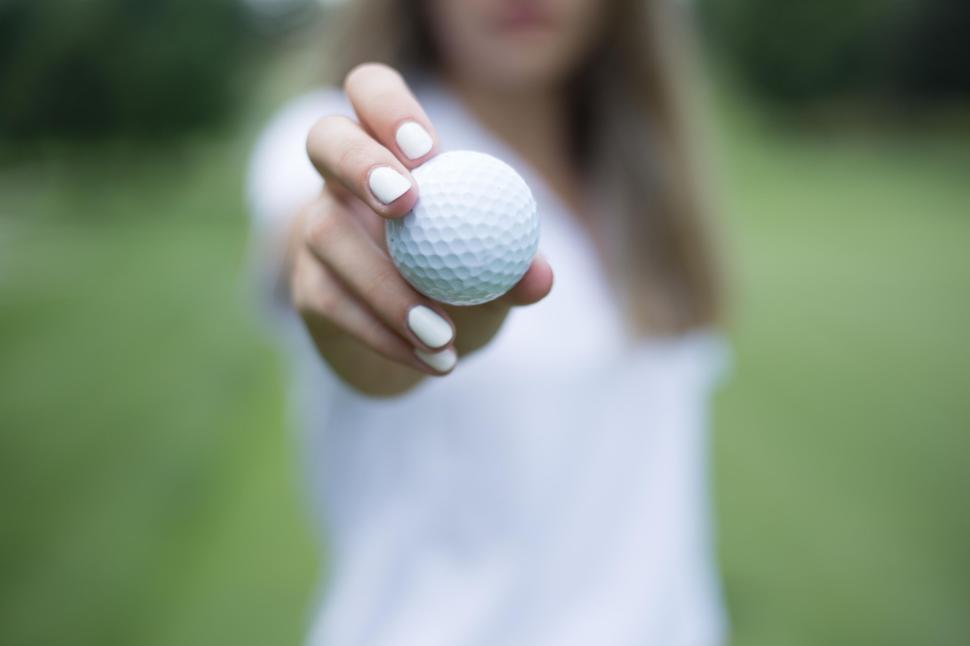 Free Image of Hand holding out a white golf ball, backdrop of a green field. 