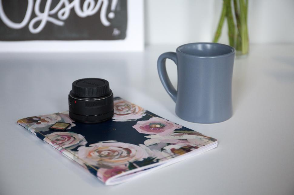 Free Image of Notebook and camera lens on desk with gray coffee mug 