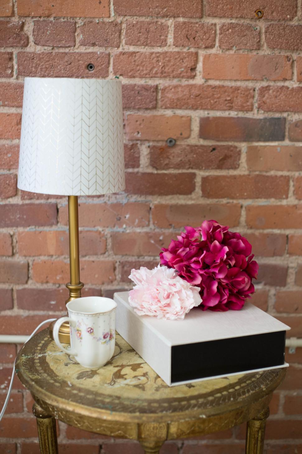 Free Image of Pink flowers and a lamp on a wooden table against a brick wall. 