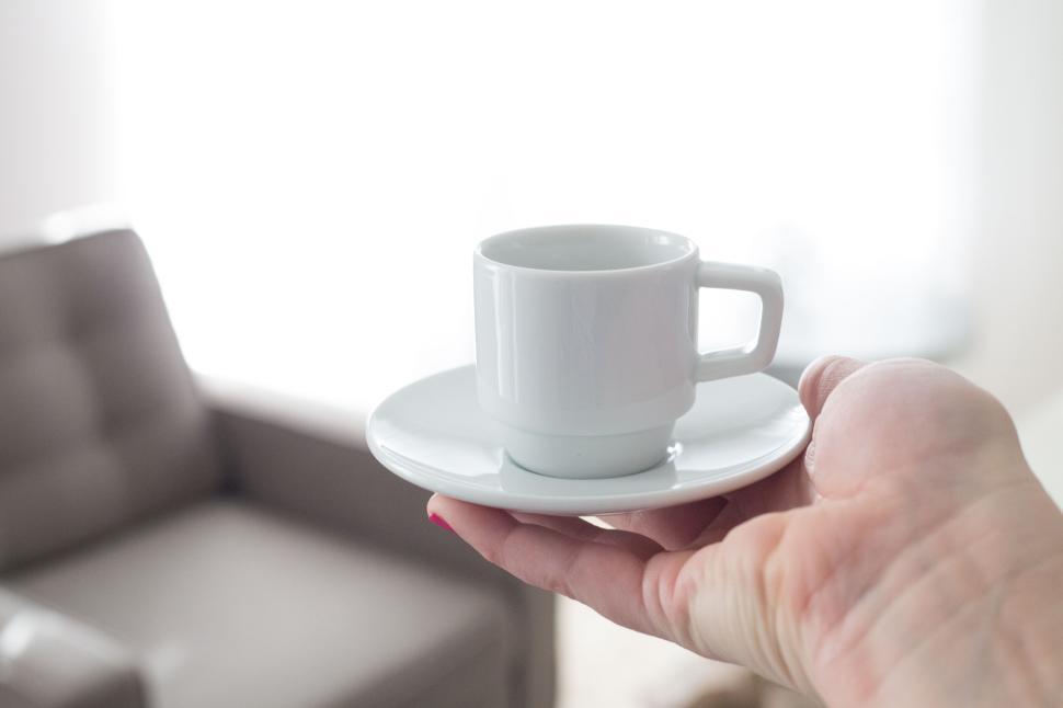 Free Image of White teacup on saucer held on hand in bright, minimalistic room 