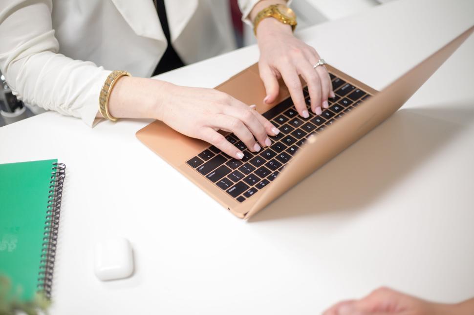 Free Image of Person typing on a laptop with green notebook and AirPods nearby 