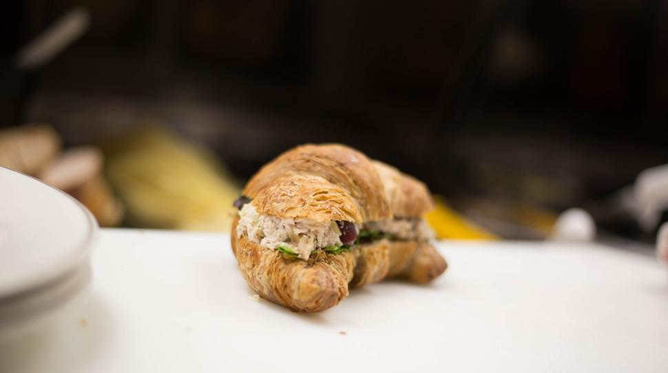Free Image of Croissant sandwich on white surface in a blurred background setting. 