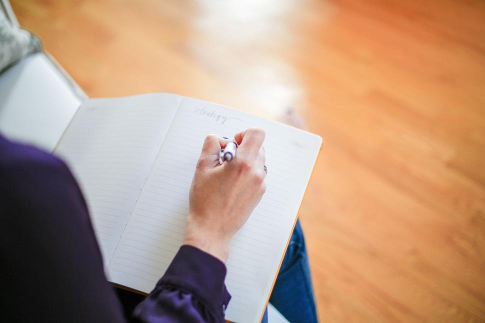 person-writing-in-a-notebook-with-pen-on-a-wooden-floor-background..jpg
