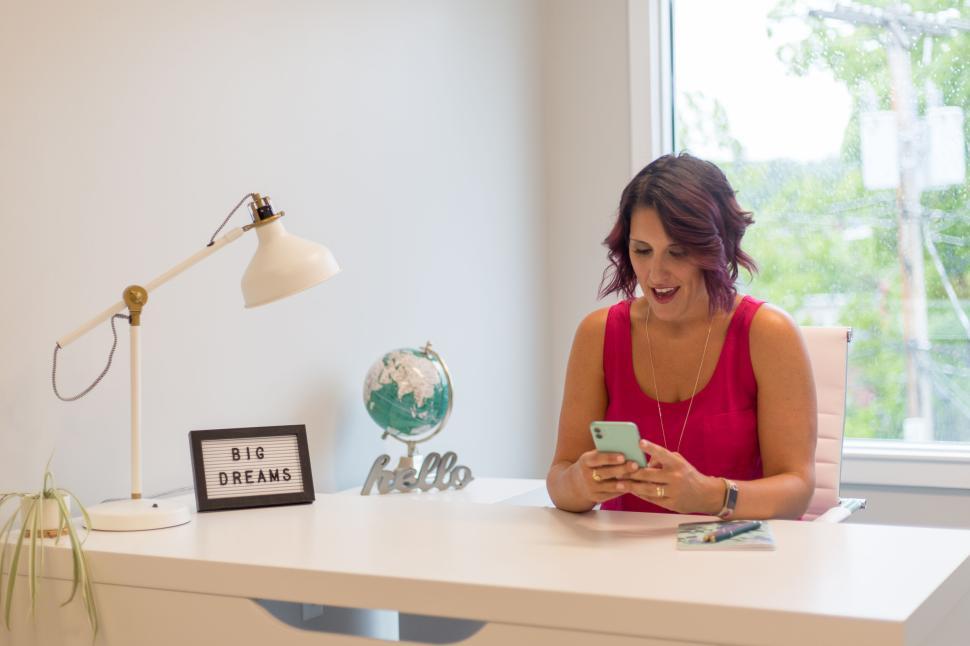 Free Image of Woman in pink dress at desk with smartphone, globe, and sign 