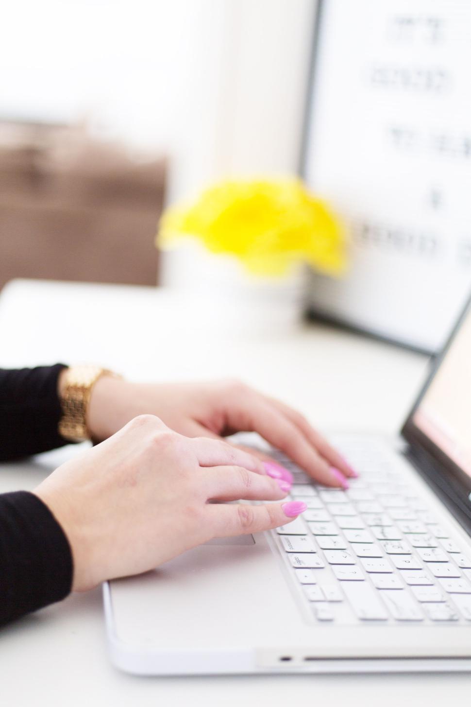 Free Image of Hands with purple nails typing on a white laptop in bright setting. 