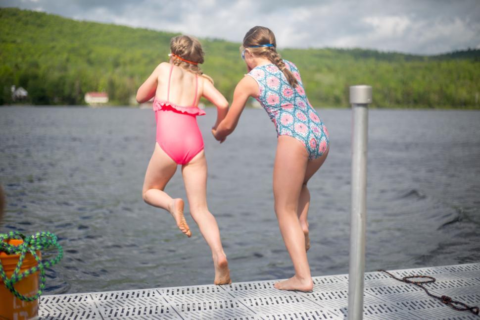 two-kids-wearing-swimsuits-jumping-off-dock-into-lake-on-sunny-day.jpg