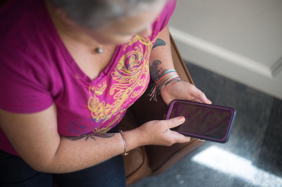 Free Image of Person holding a smartphone and sitting in pink shirt in chair 