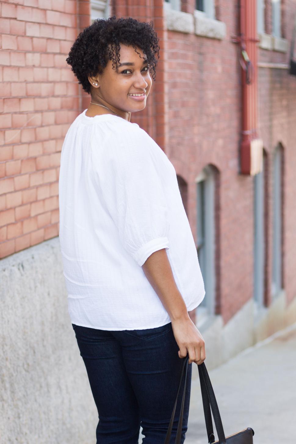 Free Image of Woman walking along brick wall holding black handbag smiling 