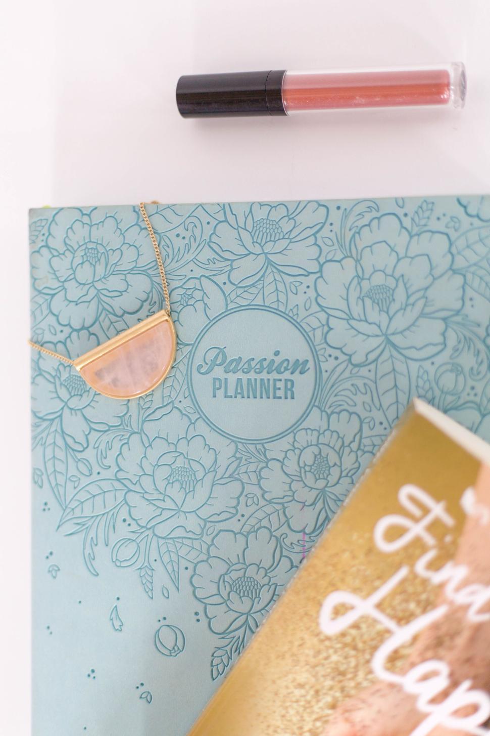 Free Image of Passion planner, gold necklace, and lip gloss on a white surface 