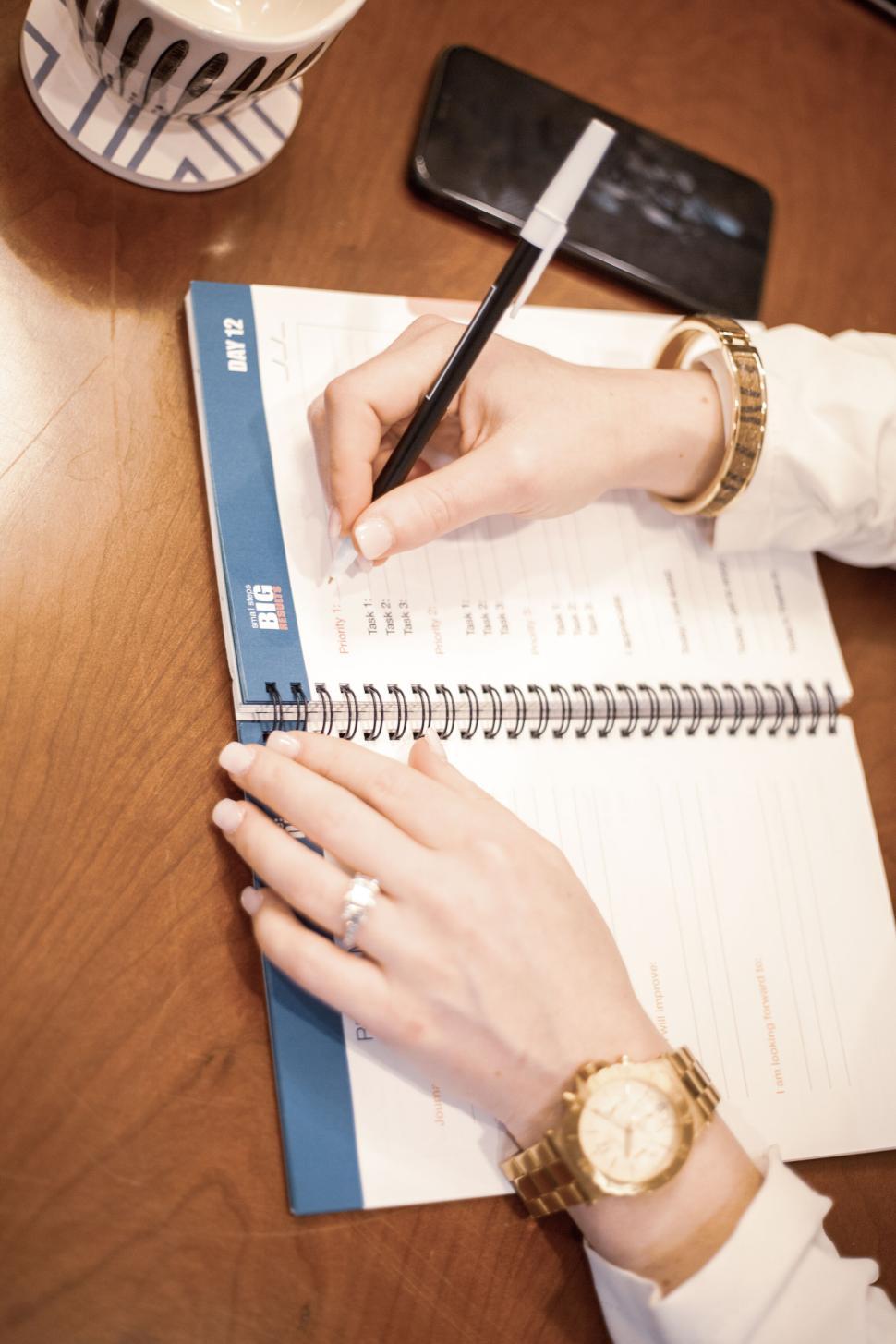 Free Image of Day planner being updated by a woman at a desk with a cup of coffee 