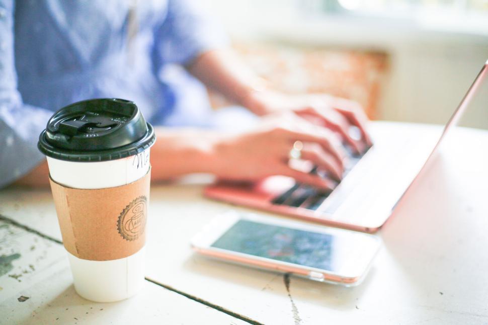 Free Image of Person typing on laptop next to a smartphone and coffee cup. 