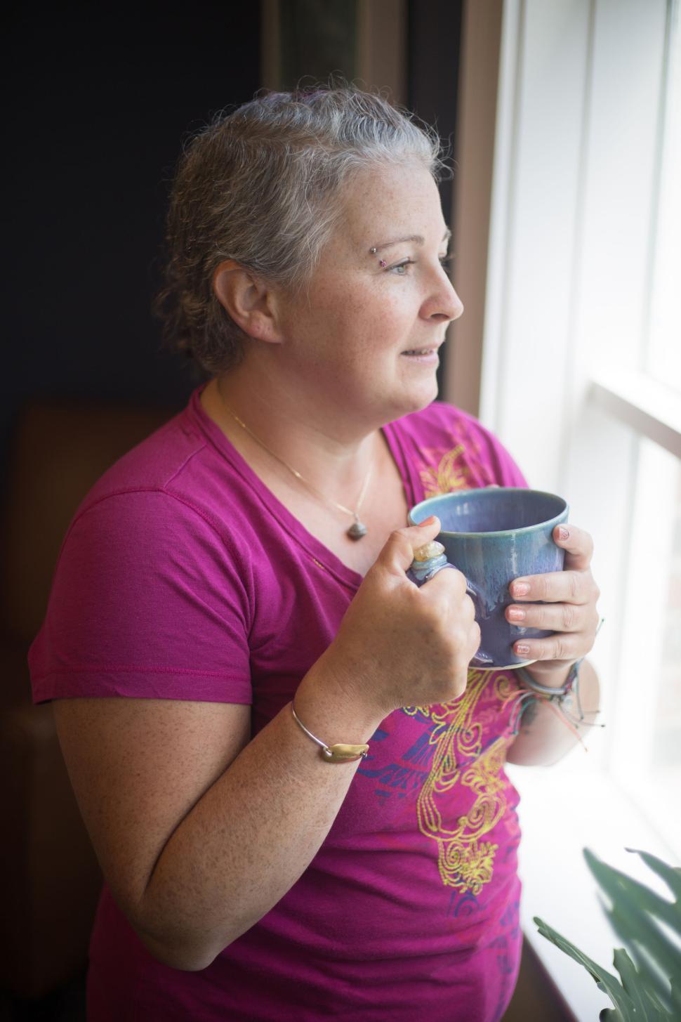 Free Image of Woman with short gray hair holding a mug and gazing outside. 
