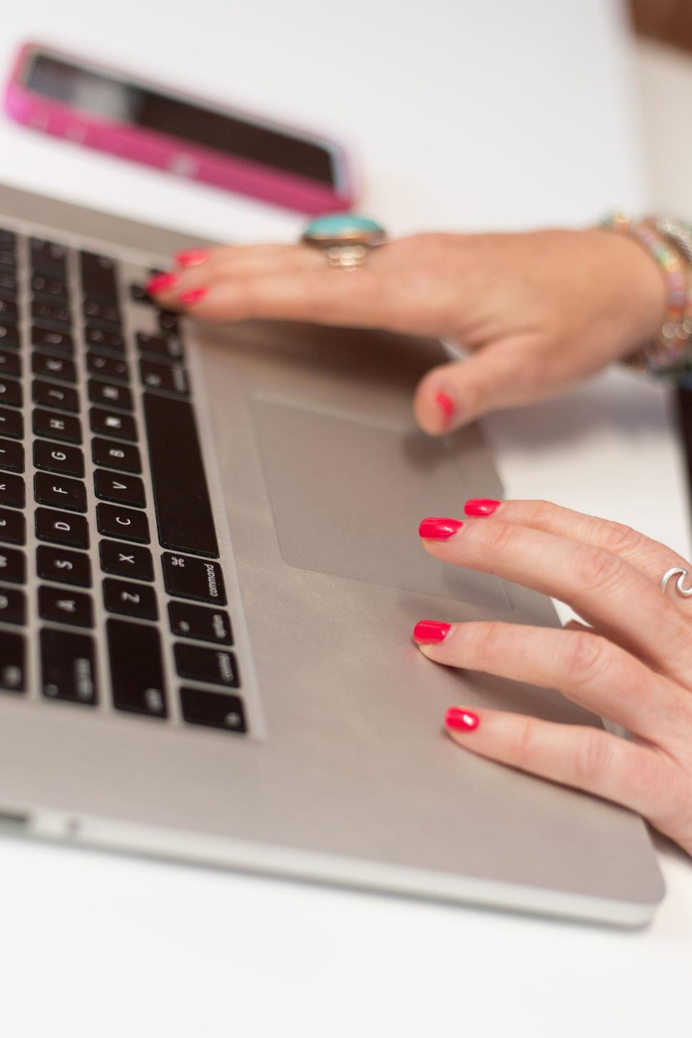 Free Image of Hands typing on a laptop keyboard with red nail polish and rings. 