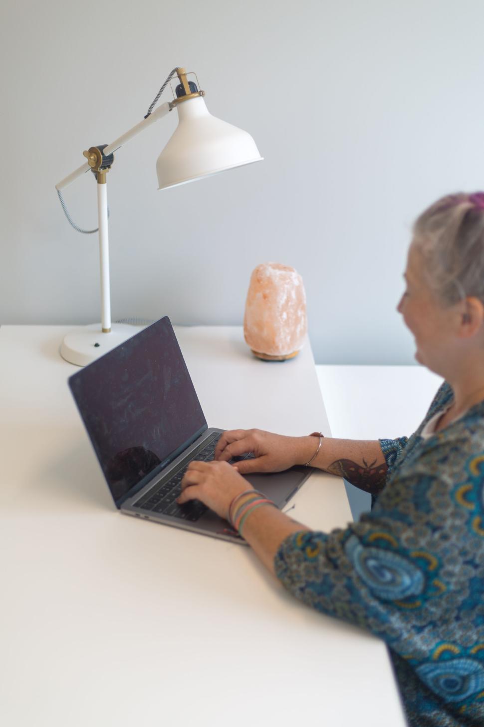 Free Image of Woman working on a laptop in minimalistic workspace with soft lighting. 