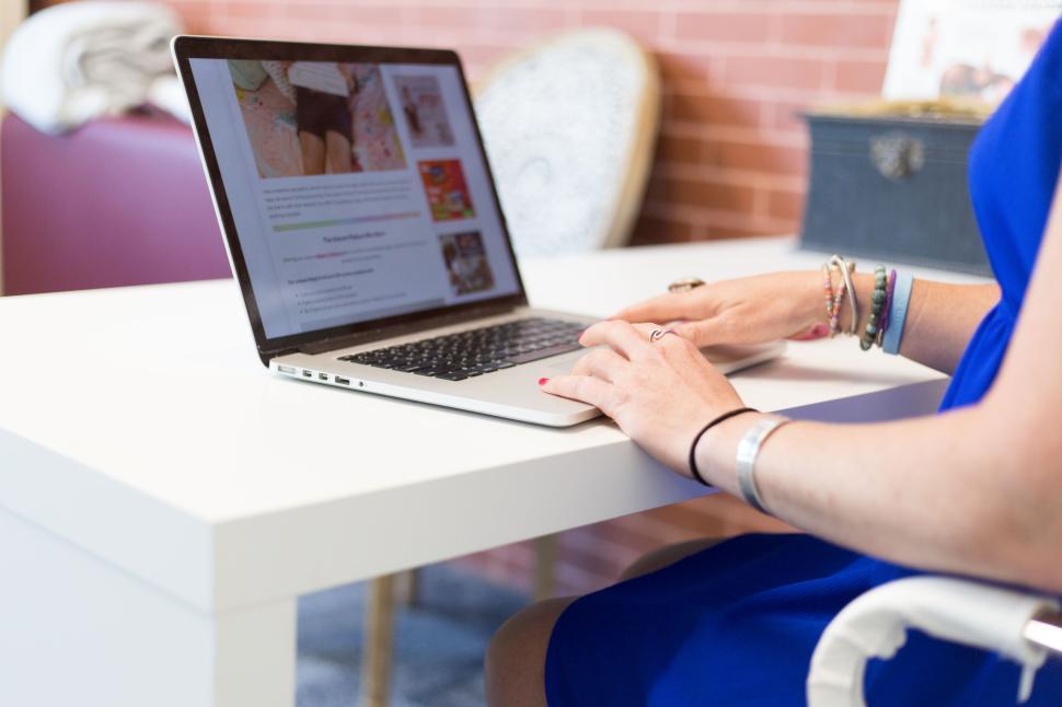 Free Image of Woman uses laptop on a white desk in a chic casual setting. 