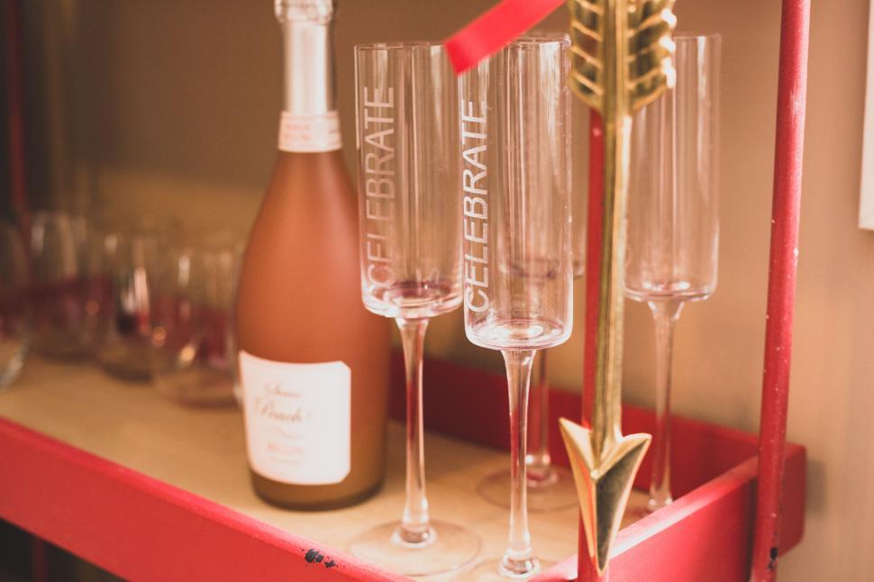Free Image of Celebrate glasses and a bottle on a red serving cart with decor. 