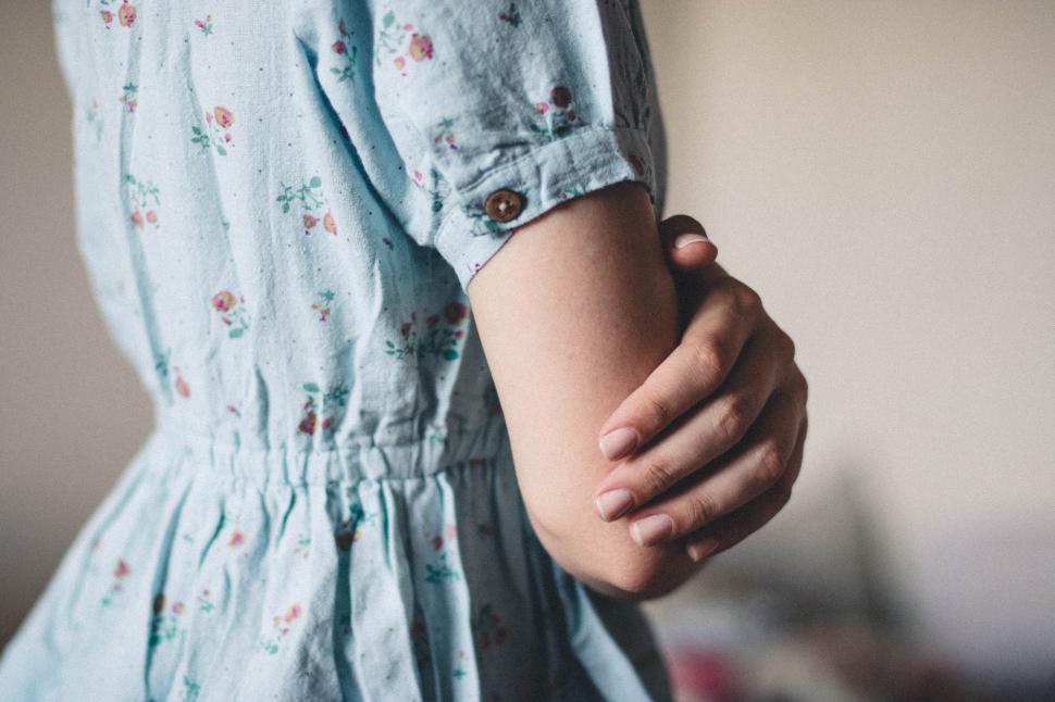 Free Image of Woman in soft blue dress holding her arm, background blurred softly. 