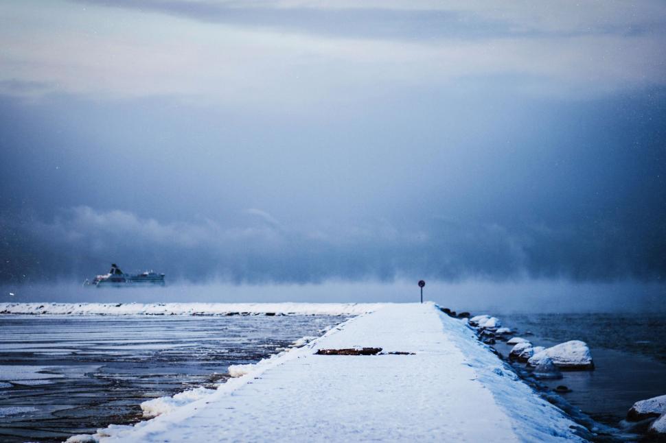 Free Image of Snow-covered pathway leading towards a foggy ocean horizon scene. 