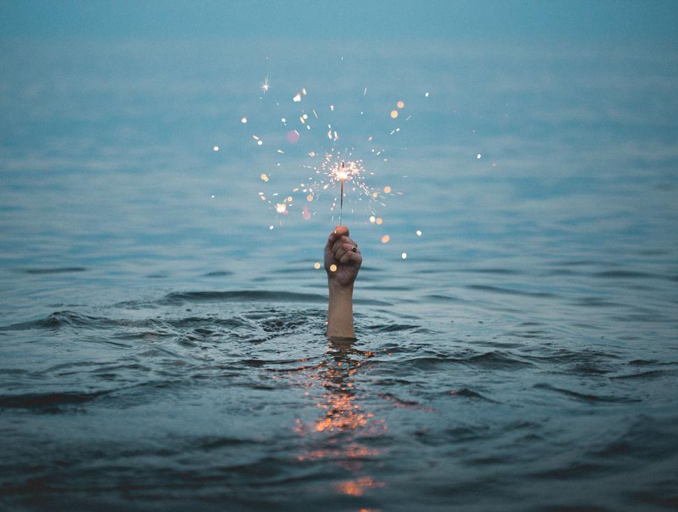 Free Image of Hand holding a sparkler above water creating a sense of wonder 