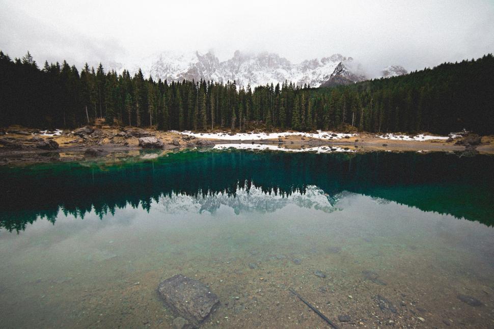 Free Image of Pristine lake with reflection of a dense forest and distant mountains 