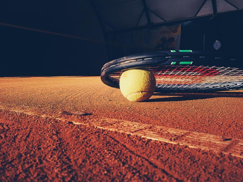 Free Image of Tennis ball resting on clay court under a racket in warm sunlight 