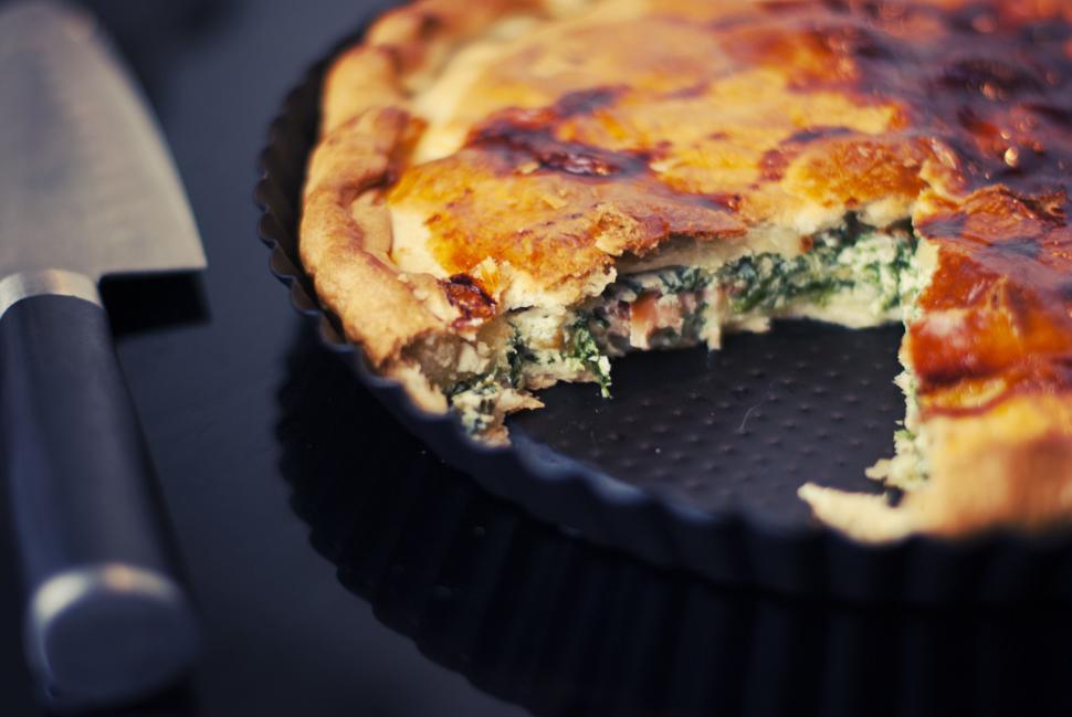 Free Image of Quiche with spinach in baking dish with a slice taken, knife beside. 
