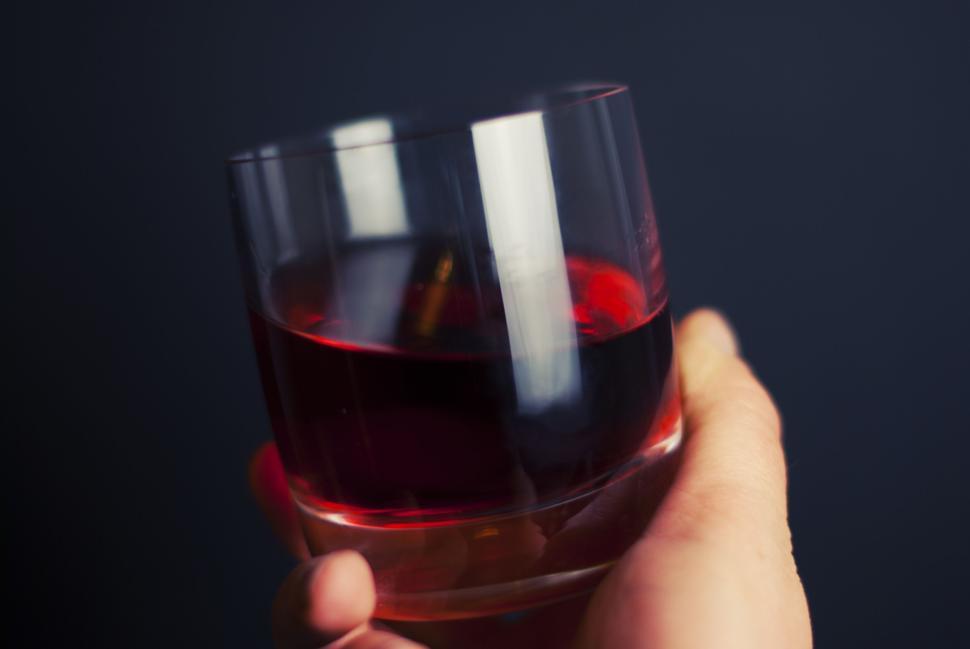 Free Image of Hand holding glass of red wine against a dark backdrop setting 