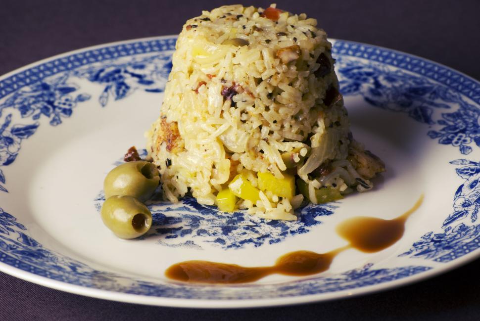Free Image of Plated gourmet rice dish garnished with olives on a floral design plate. 