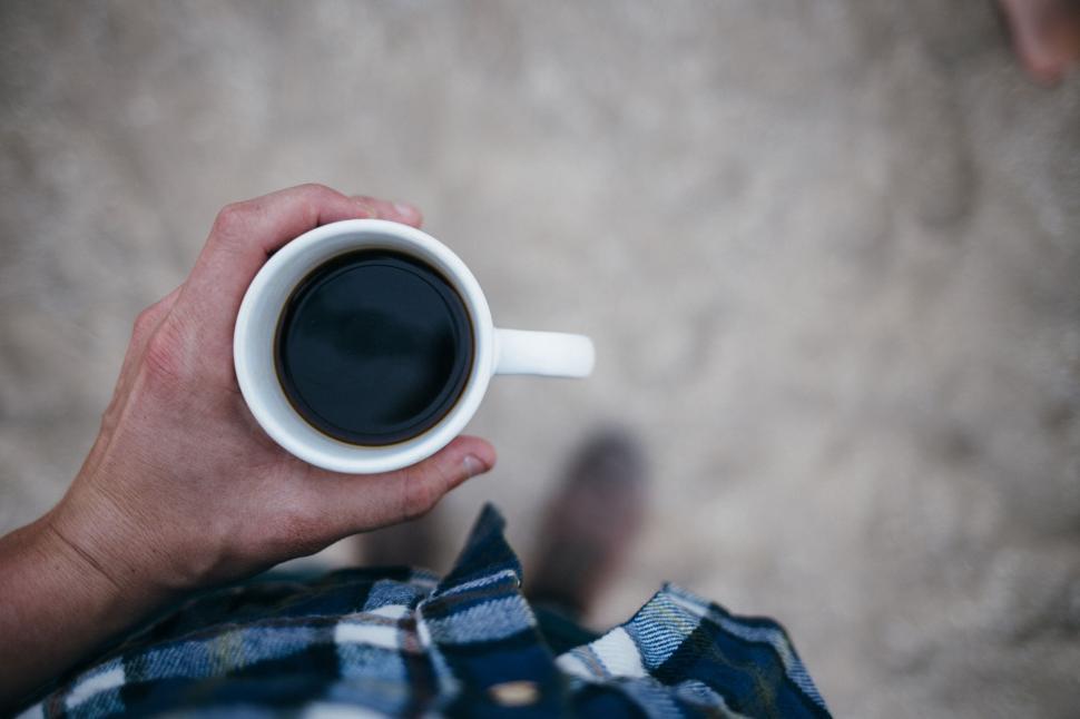 Free Image of Hand holding a cup of coffee wearing plaid outdoors on a dirt path 