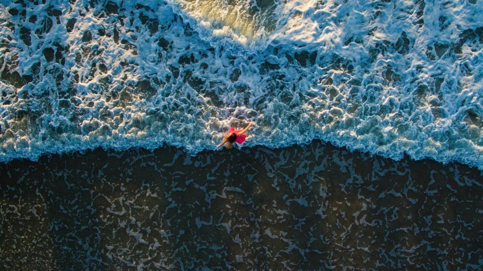 Free Image of Aerial shot of person in red shirt standing in the ocean waves. 