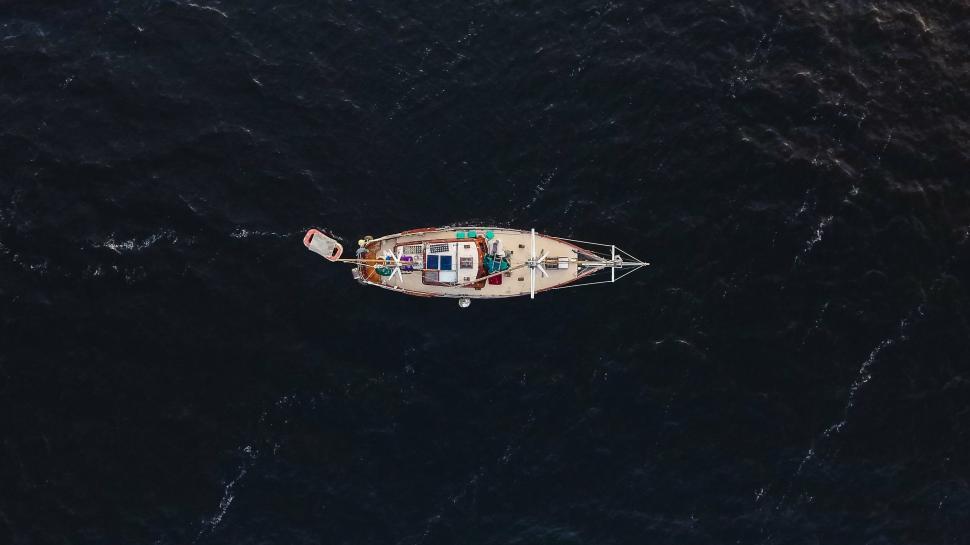Free Image of Aerial view of a lone sailboat navigating through deep blue water 