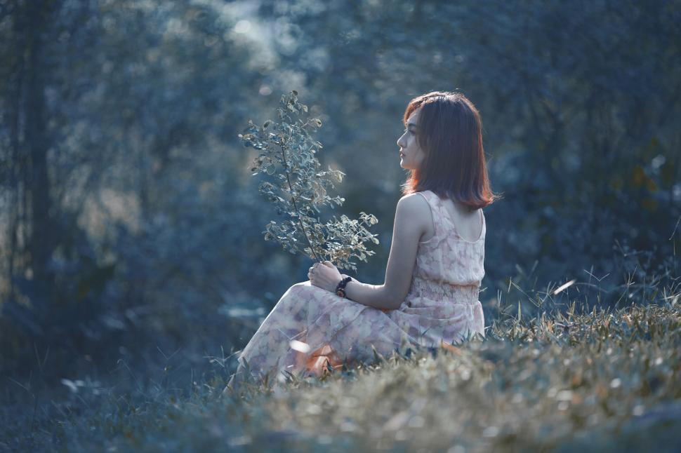 Free Image of Woman in a flowy dress sitting in a field holding wildflowers. 