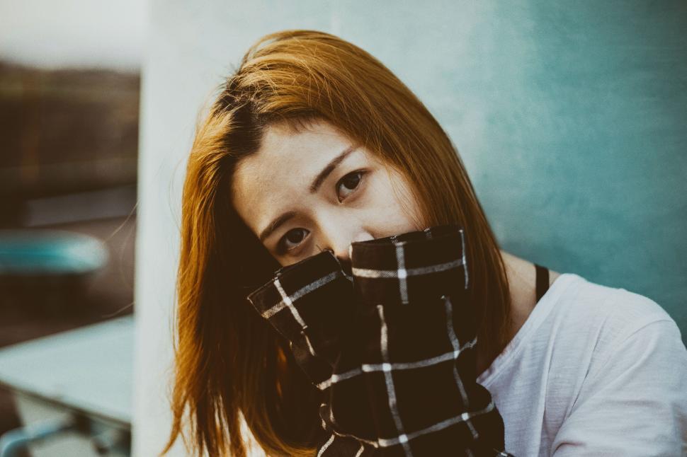 Free Image of Person in white shirt with plaid scarf covering face at outdoor location. 