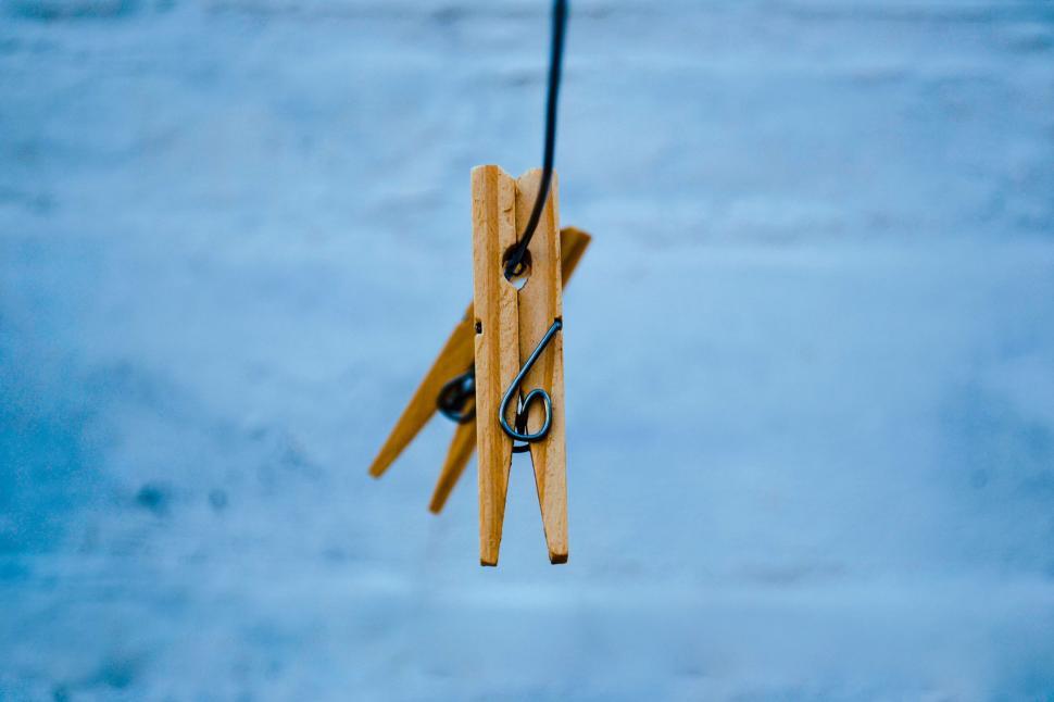 Free Image of Two wooden clothespins hanging on a black wire against blue background. 