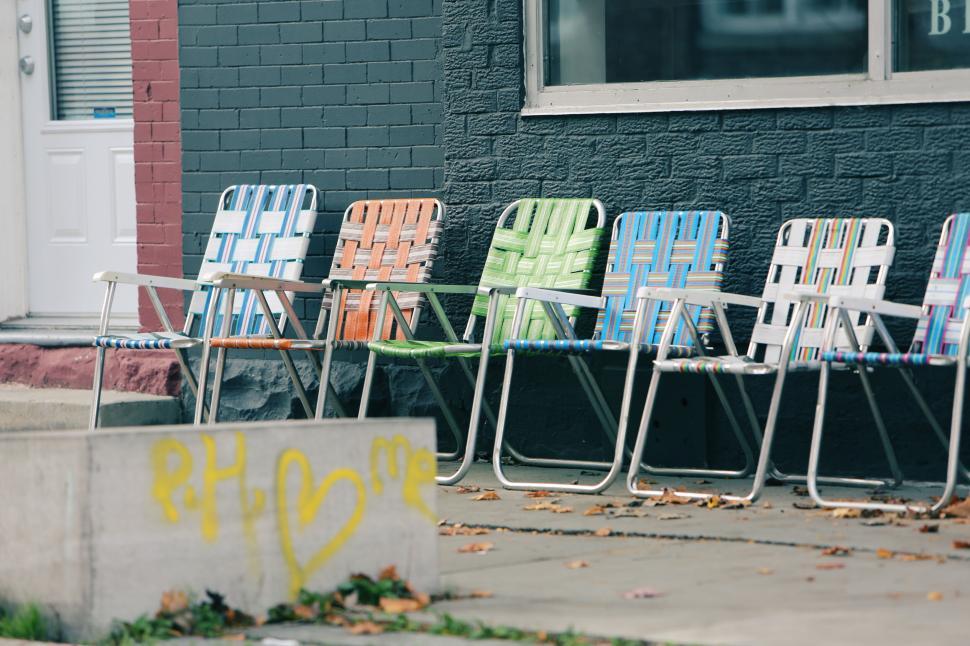 Free Image of Colorful lawn chairs lined up outside on a sidewalk next to a building. 