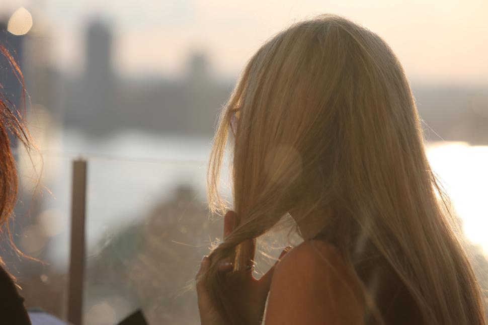 Free Image of Blonde woman in the sunlight with cityscape blurred in the background 
