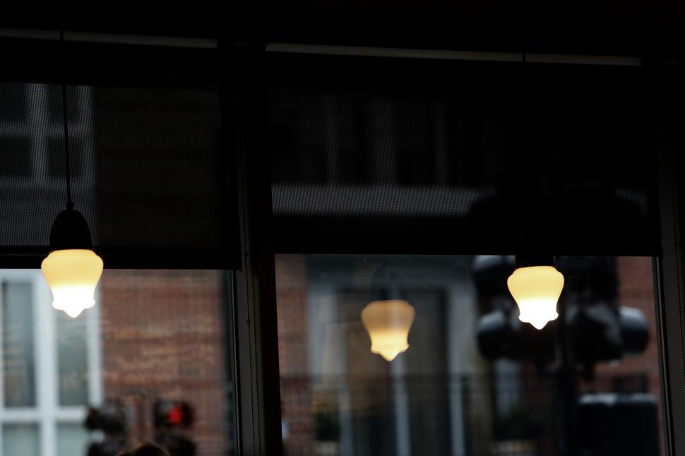 Free Image of Three hanging light bulbs reflecting in glass window with dark ambiance 