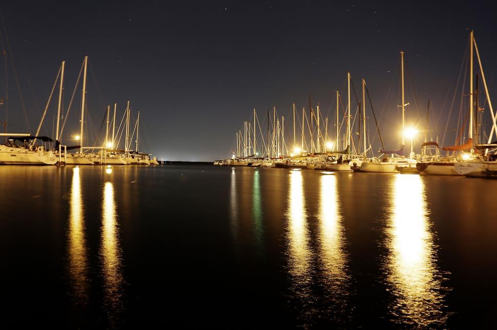 Free Image of Nighttime illuminating reflections on water from docked sailboats. 
