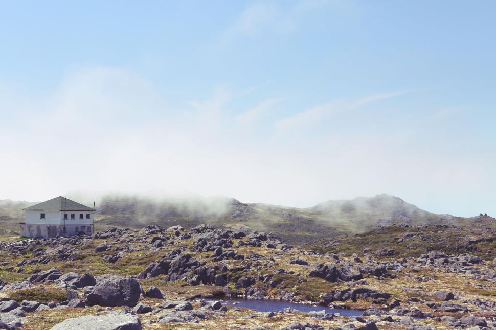 Free Image of Remote house on rocky terrain with mist and clear blue sky 