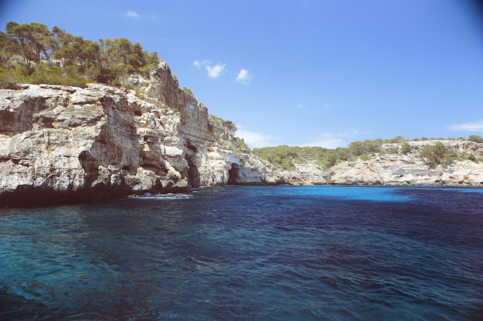 Free Image of Rocky cliff and blue waters under bright sky on a summer day scene. 
