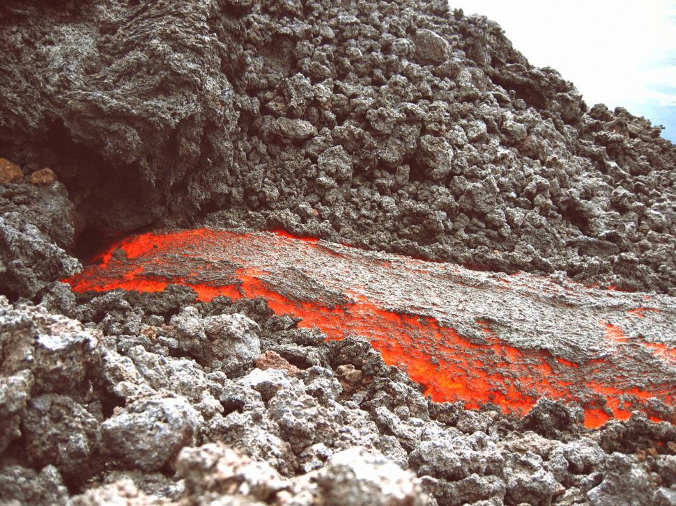 Free Image of Molten lava flowing amidst rugged volcanic rocks and terrain 