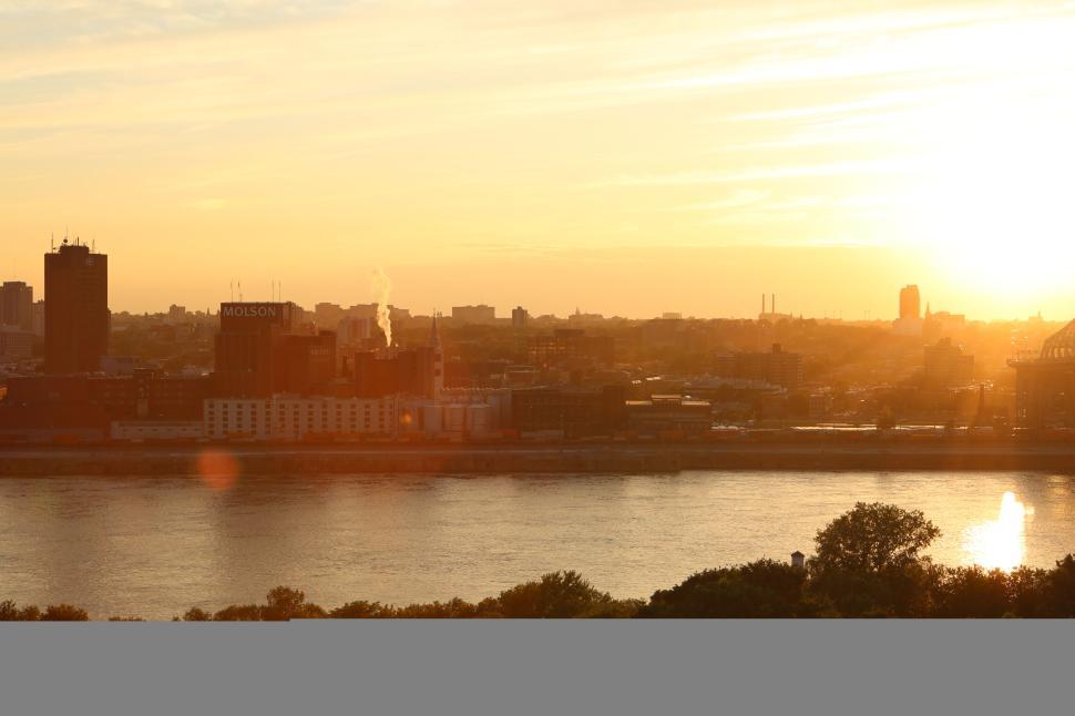 Free Image of Sunset over city skyline viewed across river with trees at the edge. 