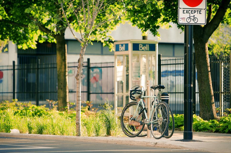Free Image of Bicycle parked by a phone booth on a sunny urban street corner. 