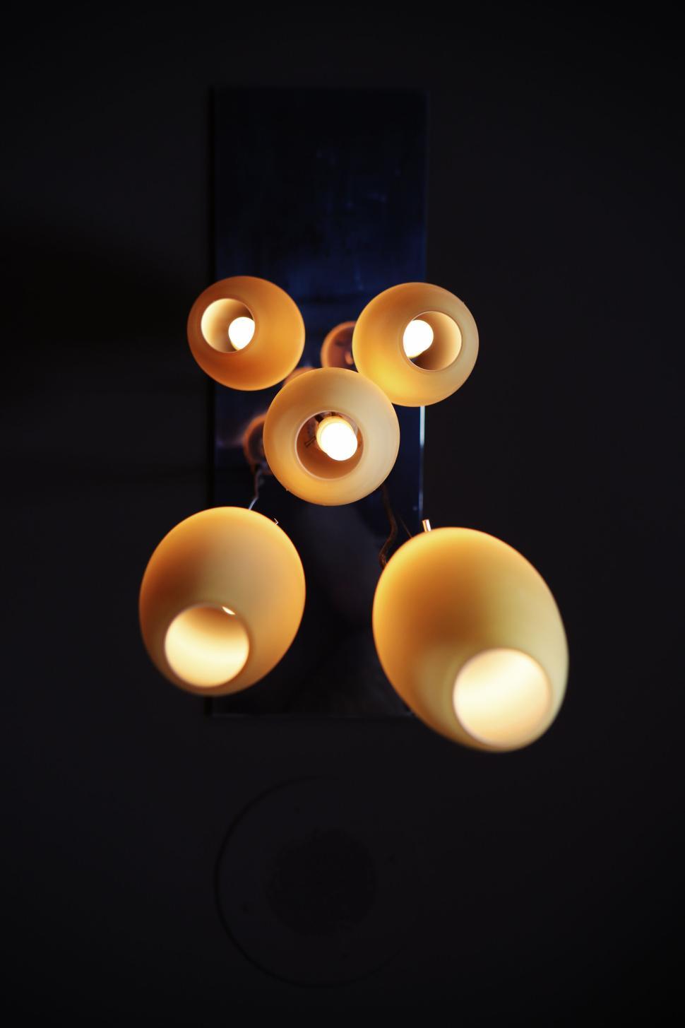 Free Image of Vertical close-up of modern ceiling lamp with glowing bulbs on dark. 
