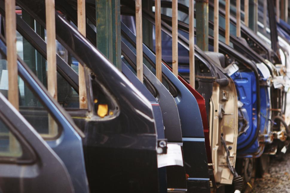 Free Image of Image of parked cars doors stacked at a junkyard behind bars 