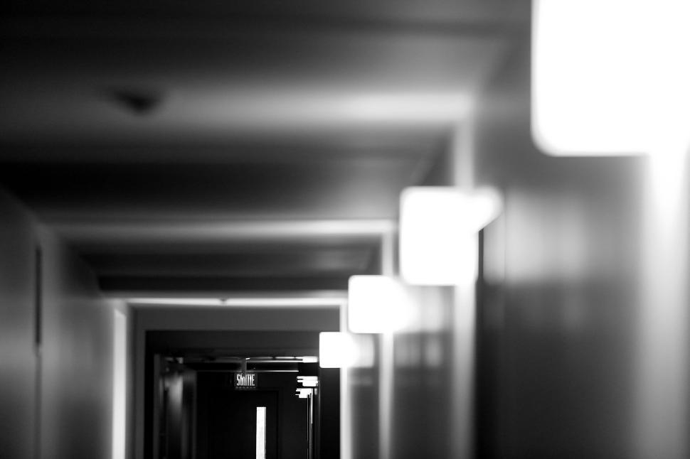 Free Image of Dimly lit corridor with light fixtures and exit sign in distance 
