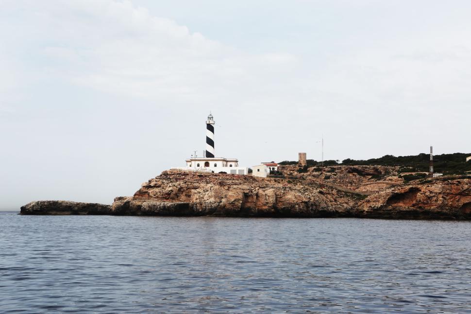 Free Image of Lighthouse on rocky cliff overlooking sea with clear sky above 
