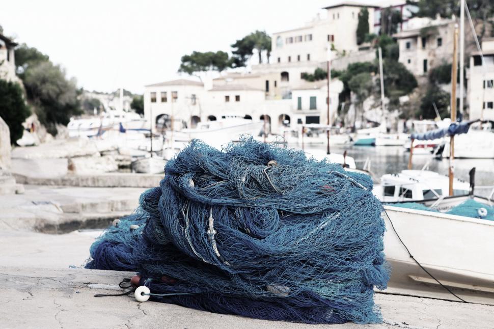 Free Image of Blue fishing nets piled on a dock in a quaint fishing village 